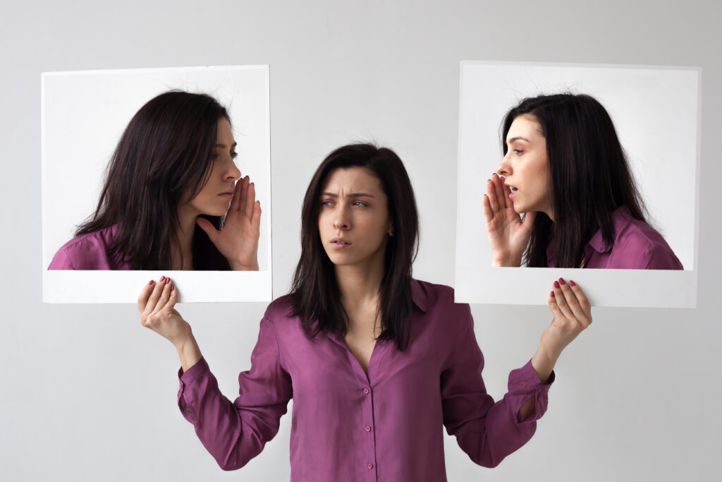 Woman holding up two photos of herself, each appearing to whisper contradictory information into her head.